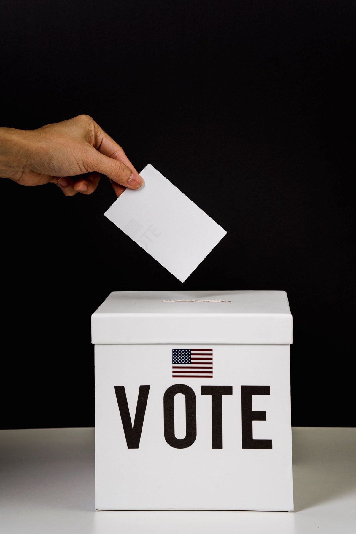 Hand placing a ballot into a box marked Vote with a US flag