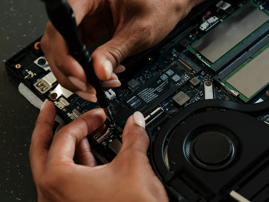 Hands using a small screwdriver to work inside an open laptop