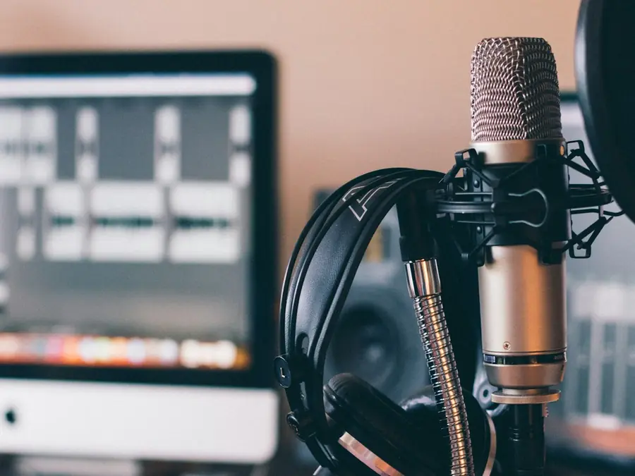 Studio microphone and headphones in front of a computer running recording software