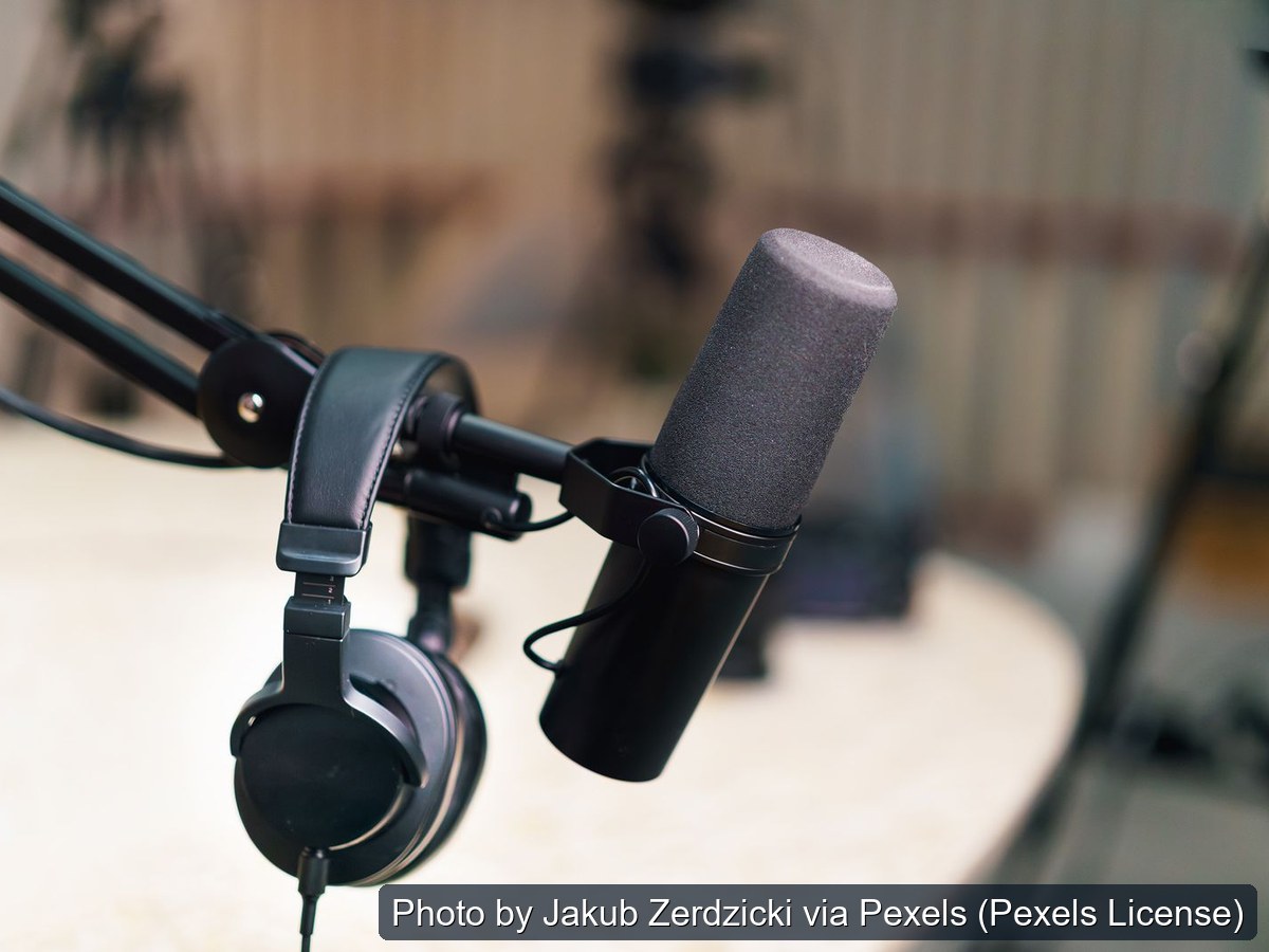 Broadcast microphone on a boom arm with headphones beside it at a studio table