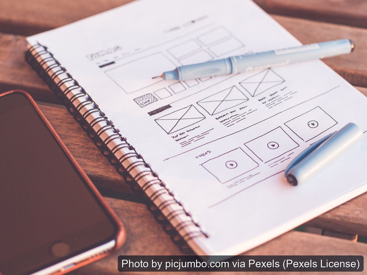 Hand-sketched website wireframe in a notebook beside a smartphone